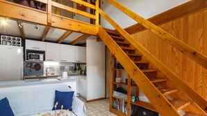 Une cuisine moderne avec des meubles blancs, un four à micro-ondes et un évier. Un escalier en bois mène à un niveau supérieur.