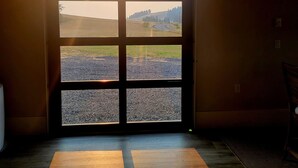 Een kamer met een groot raam, bestaande uit zes ruiten, met uitzicht op een landelijke omgeving met velden en een kronkelende weg.