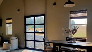 Ruime kamer met een grote schuifdeur naar een buitenruimte, een eettafel met stoelen, en een zithoek met een comfortabele bank.