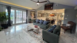 A spacious living room with a large sliding glass door, a ceiling fan, and a dining area with chairs and a table. - Cozy 4BR Home with Office, Fitness Area, Spacious Backyard & Pet-Friendl (Monroe)