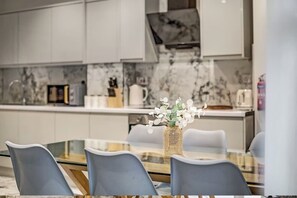 Une cuisine moderne avec des meubles blancs, un pare-feu en marbre et un coin repas comprenant une table et des chaises en verre.