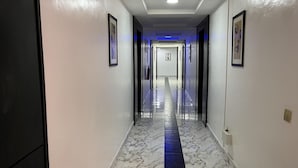 Een gang met een marmeren vloer, ingelijste foto's aan de wanden en een blauw verlicht plafond.