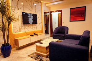A modern living room with a marble wall, a mounted TV, a blue sofa, and a potted plant. - 2-Bedroom Flat Lekki Phase 1 - Pool - Spa (Lekki)
