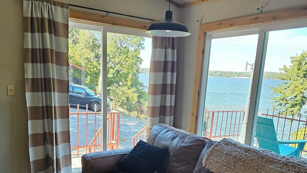 Una sala de estar acogedora con un sofá de cuero marrón, una cortina estampada y vistas a una masa de agua a través de amplias ventanas.