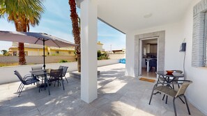 An outdoor patio with a table and chairs, a palm tree, and a view of a building in the background. - Sucina 3-Bed Villa, Sleeps 6 & Pet Friendly (Sucina)