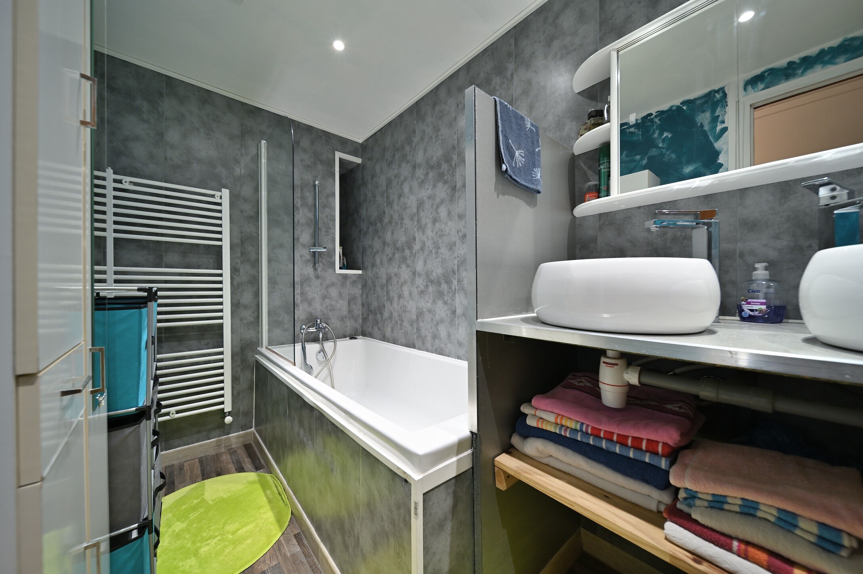 A modern bathroom with a bathtub, a shower, a towel rack, and a shelf with toiletries.