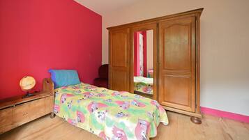 Een slaapkamer met een houten garderobe, een bed met een kleurrijk sprei, een bureau met een wereldbol en een rode muur.