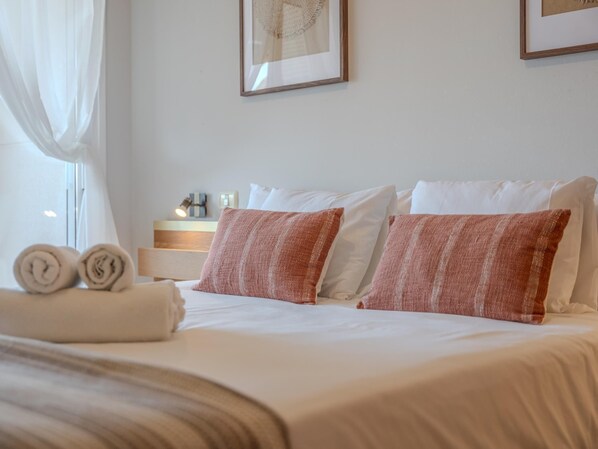 A neatly made bed with white and brown striped pillows, a rolled towel, and a bedside table with a lamp and a small box.
