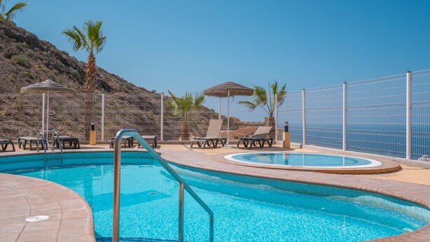 A swimming pool with a curved edge, surrounded by lounge chairs and a fence. - Sunset, Apartment in Costa Adeje - Relax in Paradise (Costa Adeje)