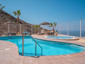 A swimming pool with a curved edge, surrounded by lounge chairs and a fence.