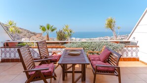 A terrace with a table and chairs, overlooking a coastal view with palm trees and a distant cityscape. - Sunset, Apartment in Costa Adeje - Relax in Paradise (Costa Adeje)