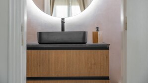A bathroom vanity with a black sink, a wooden cabinet, and a round mirror.