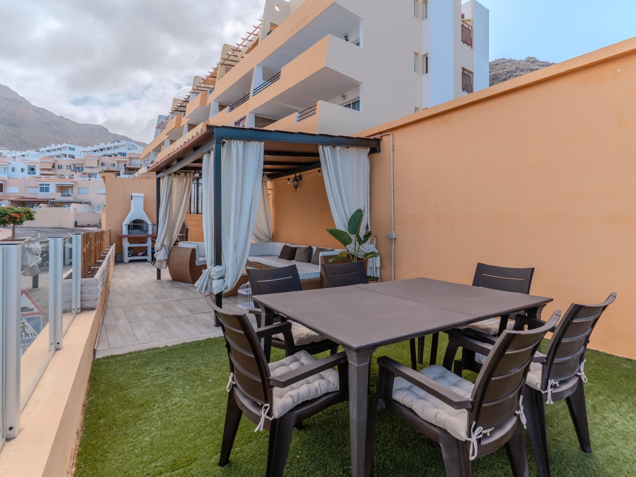 An outdoor patio with a table and chairs, a grill, and a seating area with a view of the cityscape and mountains in the background.