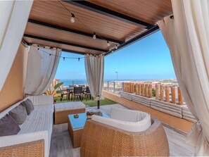 A balcony with wicker furniture, a table, and curtains. - Sol del Conde Holiday Apartment: Your Retreat in Costa Adeje (Costa Adeje)