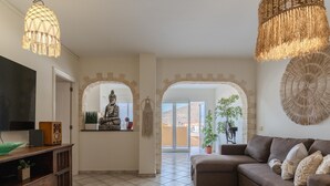 A living room with a sofa, a TV, a Buddha statue, and a macrame wall hanging.