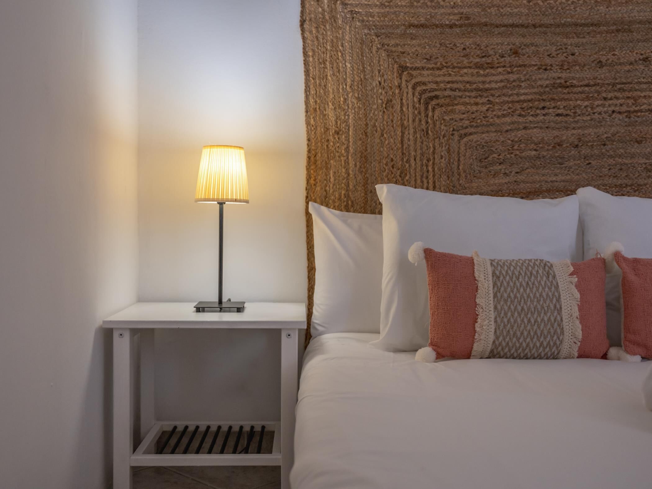 A neatly made bed with white and pink pillows, a bedside lamp, and a textured wall behind it.