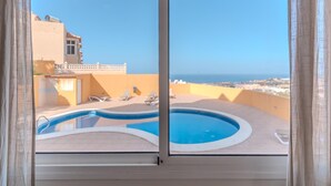 A pool area with lounge chairs, a clear sky, and a distant view of the sea.