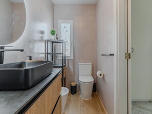 A compact bathroom with a modern sink, toilet, and a small trash bin.