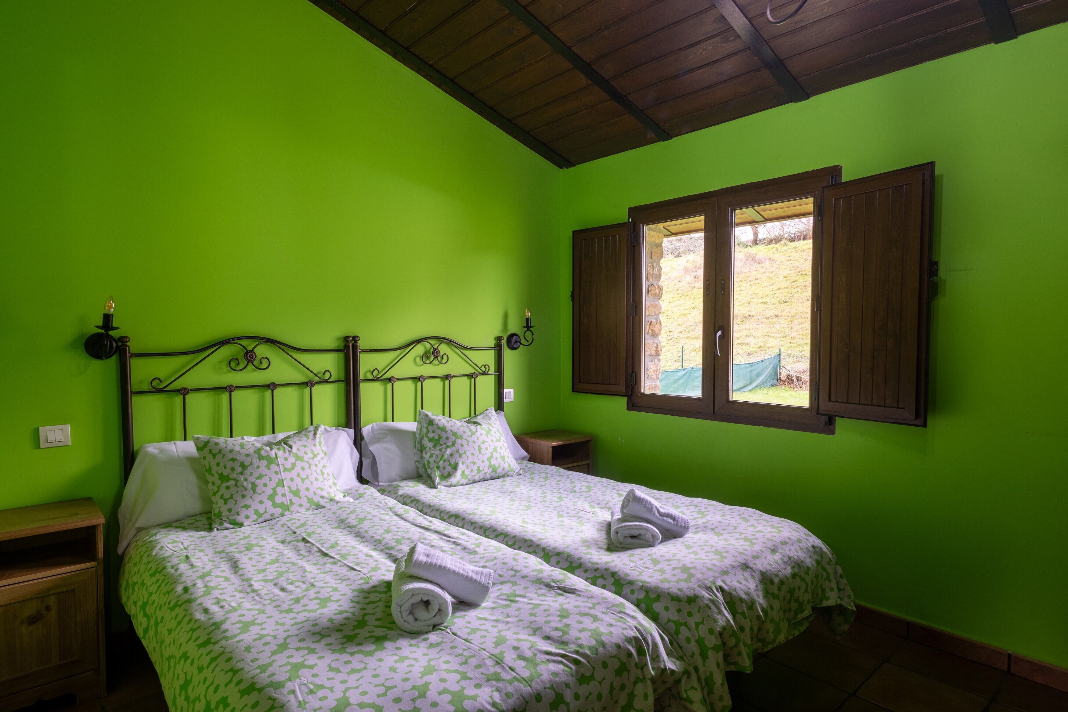 Une chambre avec deux lits, une tête de lit en bois, une fenêtre avec des volets en bois et un mur vert.