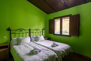 A room with two beds, a wooden headboard, a window with wooden shutters, and a green wall.