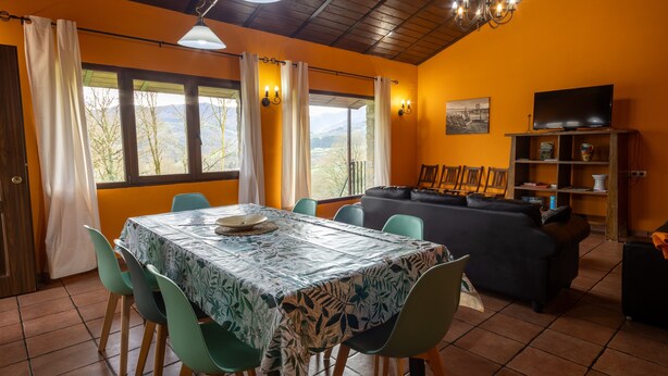 Un área de comedor con una mesa y sillas, un sofá, un televisor y una estantería.