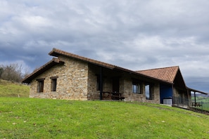 A stone building with a sloped roof, a porch, and a grassy hill in the foreground.