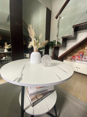Un intérieur moderne avec une table ronde en marbre, deux vases décoratifs et une bibliothèque contenant des livres et un jeu de société.