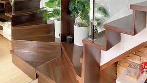 A wooden staircase with glass railings, white walls, and potted plants. - Cozy 2-bedroom condo in charming BGC Taguig with AC, WiFi Netflix WashingMachine (Taguig)