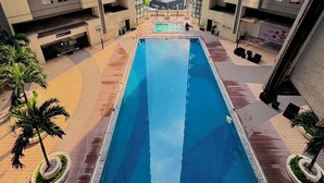 A swimming pool surrounded by a courtyard with palm trees, between high-rise buildings. - Cozy 2-bedroom condo in charming BGC Taguig with AC, WiFi Netflix WashingMachine (Taguig)