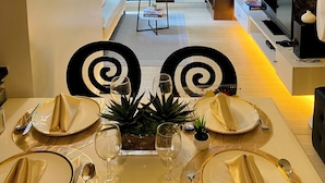A modern dining area with a table set for two, a sofa in the background, and a staircase leading to an upper level. - Cozy 2-bedroom condo in charming BGC Taguig with AC, WiFi Netflix WashingMachine (Taguig)
