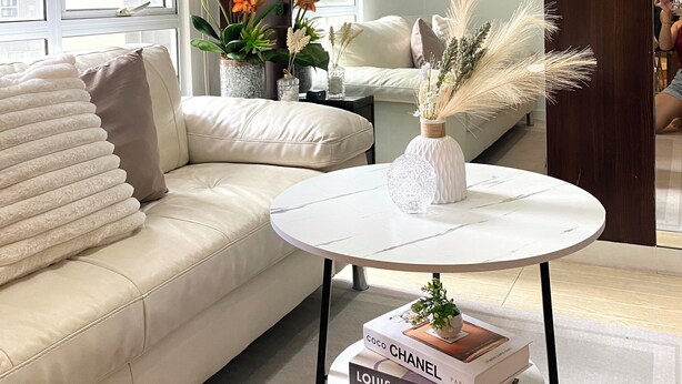 A modern living room with a beige sofa, a round coffee table with books, and decorative plants. - Cozy 2-bedroom condo in charming BGC Taguig with AC, WiFi Netflix WashingMachine (Taguig)