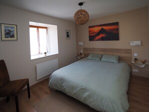 A bedroom with a bed, a window with curtains, a wall-mounted lamp, and a painting.
