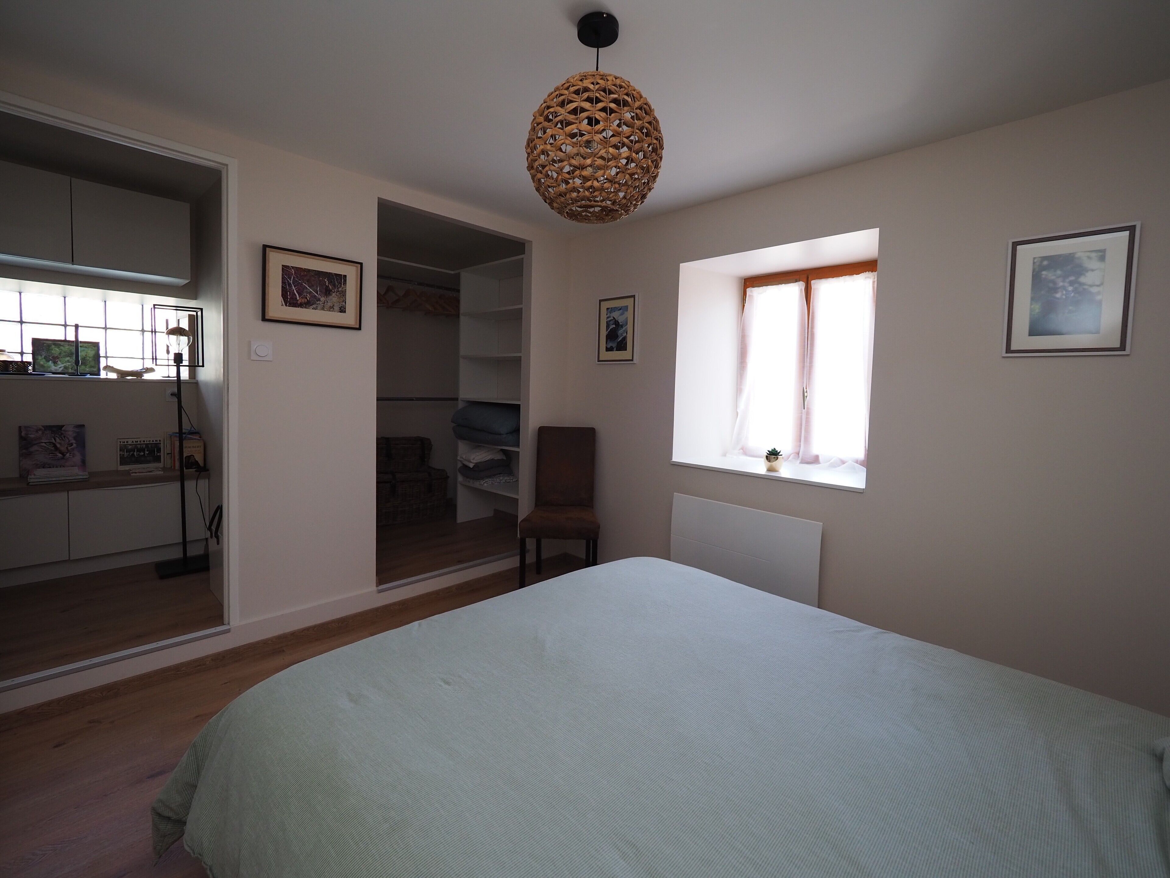 Ein Schlafzimmer mit Bett, einem fenster mit Vorhängen, einem Stuhl, einem Kleiderschrank und einer Deckenleuchte.