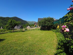 A grassy yard with a stone wall, a tree, and a building with a sloped roof.