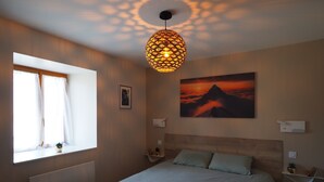 A bedroom with a bed, a window with curtains, a wall-mounted picture, a ceiling light fixture, and bedside tables. - Apartment 'La Grange' with Mountain View, Private Garden and Wi-Fi (Cazeaux-de-Larboust)