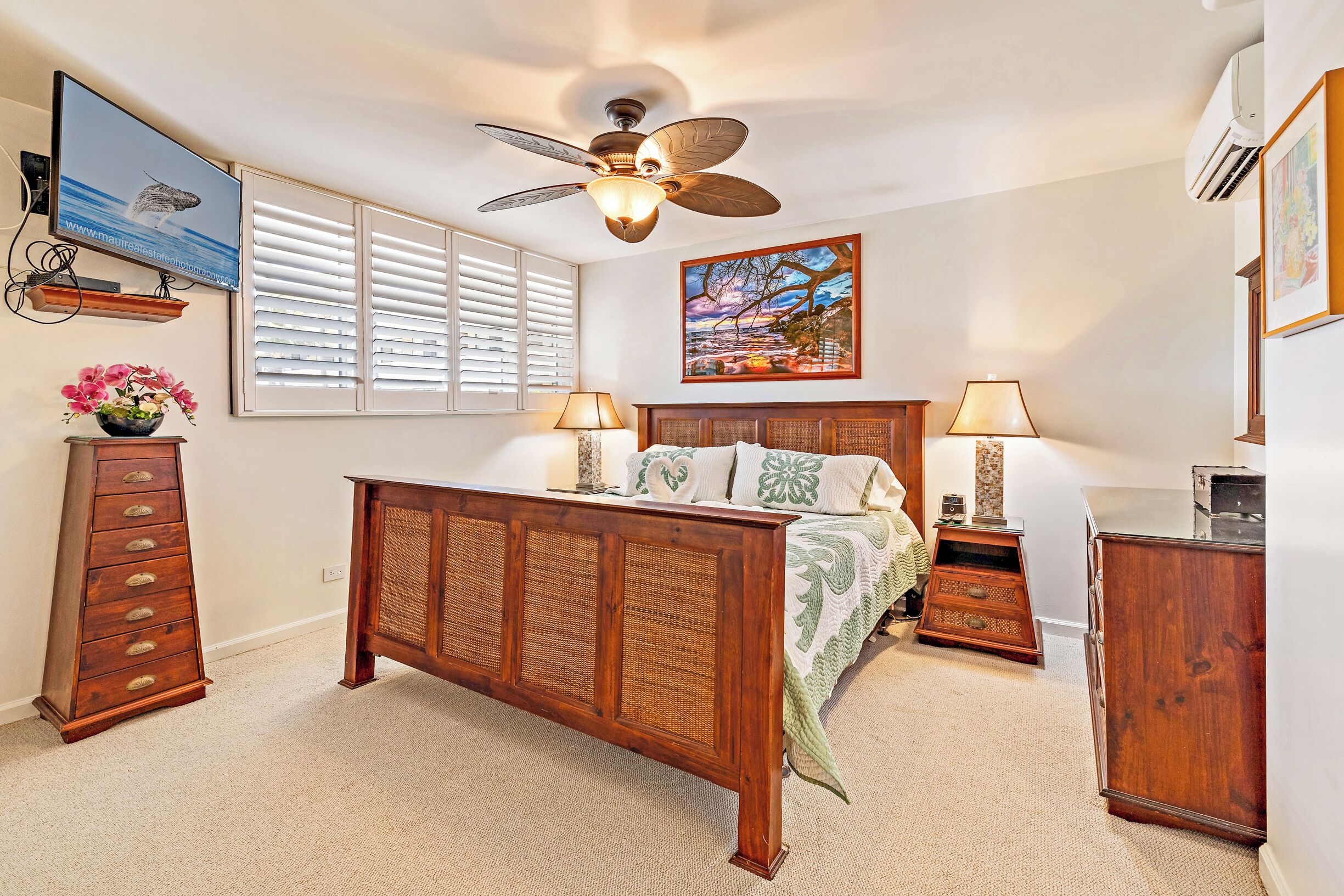 A bedroom with a wooden bed, a ceiling fan, a TV, and a painting on the wall.