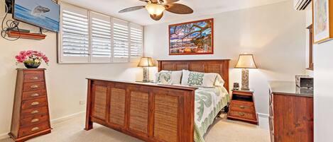 A bedroom with a wooden bed, a ceiling fan, a TV, and a painting on the wall.
