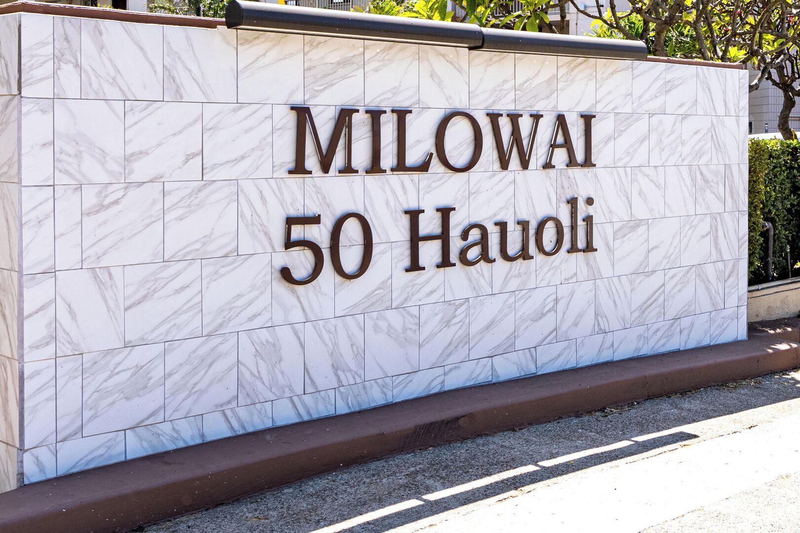 Ein Schild mit dem Schriftzug 'MILOWAI 50 HAUOLI' an einer Marmorwand.