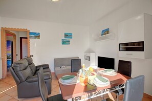Una sala de estar moderna con sofá, mesa de comedor y sillas. Hay estanterías y un televisor de pantalla plana.