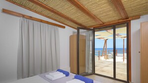 Un dormitorio con cama, puerta corrediza al balcón y vista al mar.