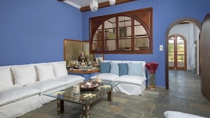 Una sala de estar con un sofá blanco, una mesa de centro de vidrio y un ventanal con marco de madera.