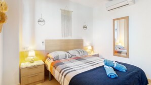 Un dormitorio con cama, lámparas de noche, ventilador de techo, aire acondicionado de pared y un espejo.