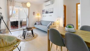 Una sala de estar moderna con un sofá, una mesa de comedor y sillas. Hay un ventilador de techo, una lámpara y una ventana con cortinas.
