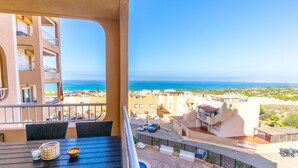 Un balcón con vistas al mar, una piscina y un área de comedor con sillas y una mesa.