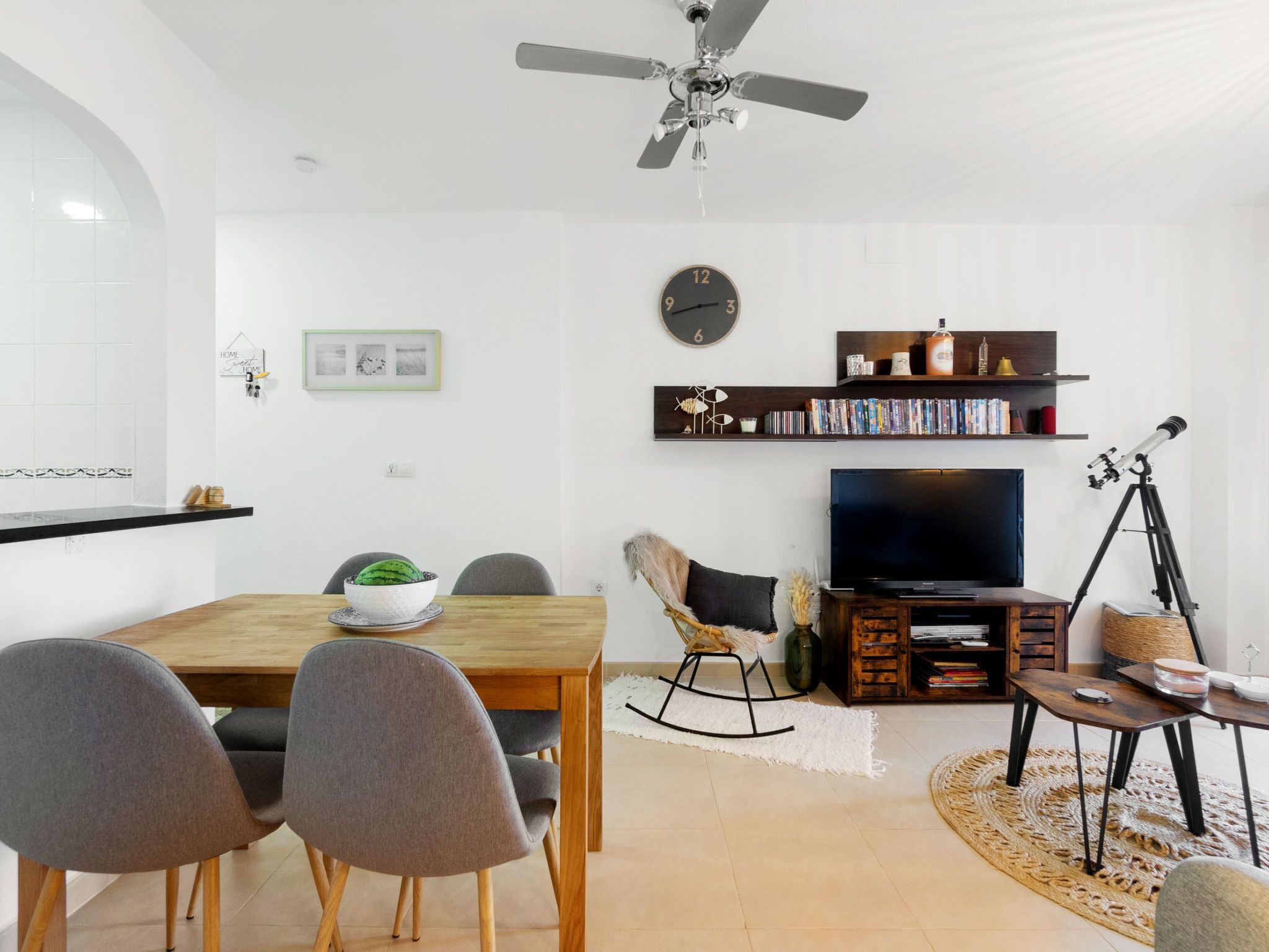 Una sala de estar moderna con comedor, ventilador de techo, estantería, televisor y un telescopio.