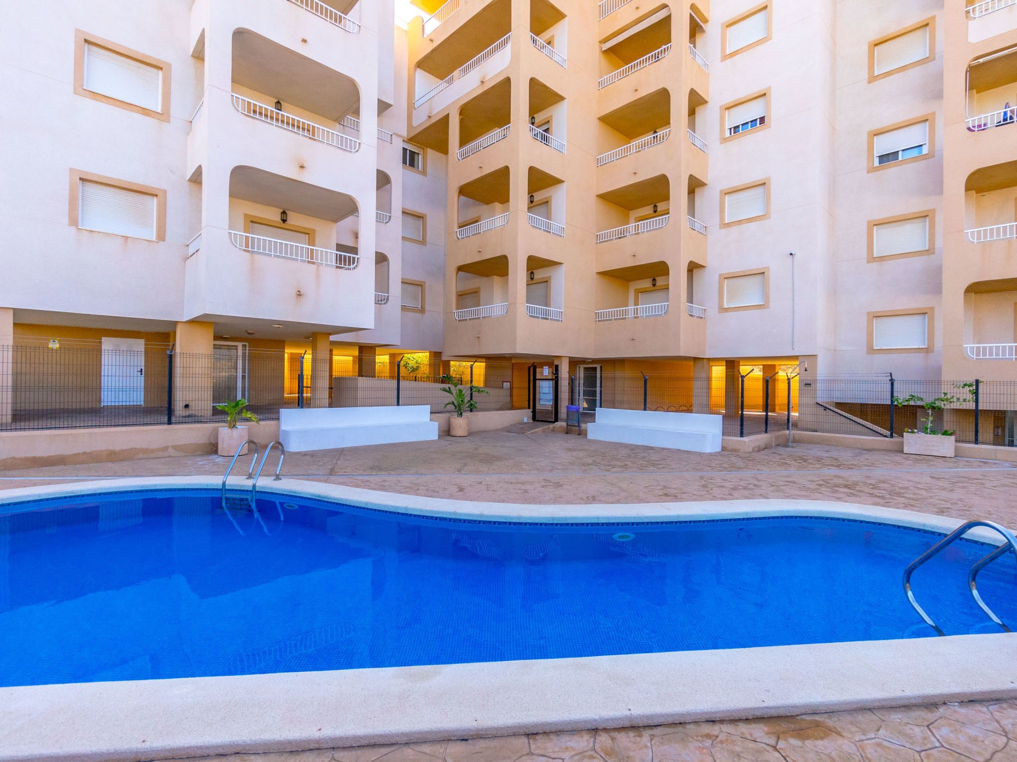 A multi-story hotel with a central courtyard featuring a swimming pool, balconies, and a covered area with seating.