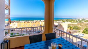 Un balcón con mesa y sillas, con vista a un pueblo costero y al mar.