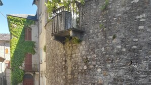 A stone building with a metal balcony, a cobblestone path, and a gravel area. - Apartment 'La Vista Sul Castello' with Mountain View, Wi-Fi and Air Conditioning (Compiano)