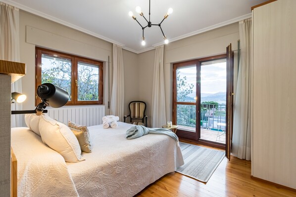 A bedroom with a large bed, a desk, a chair, and a view through a sliding door.