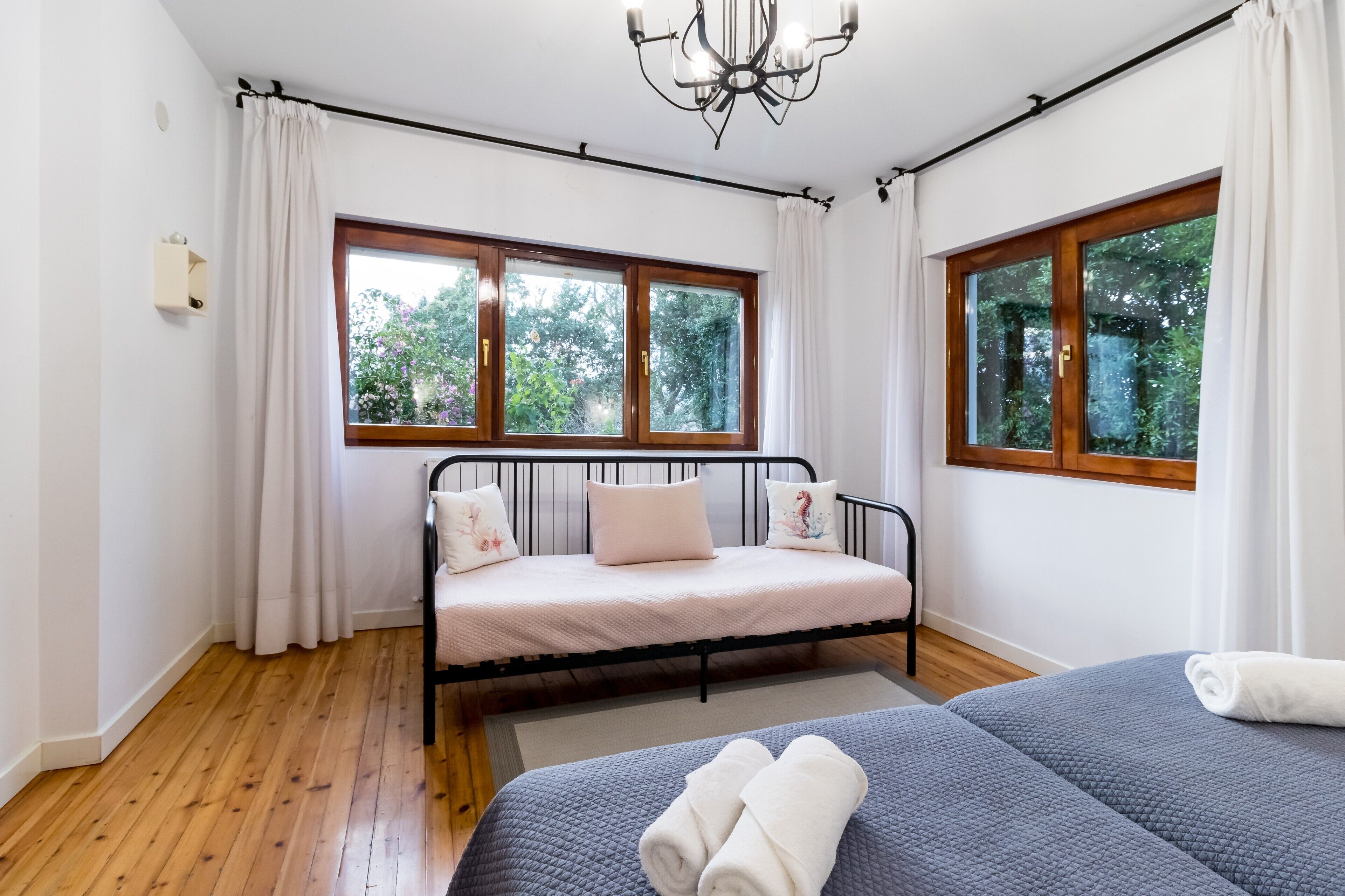 Une chambre avec un lit, une fenêtre avec des rideaux, un lustre et une vue sur les arbres.